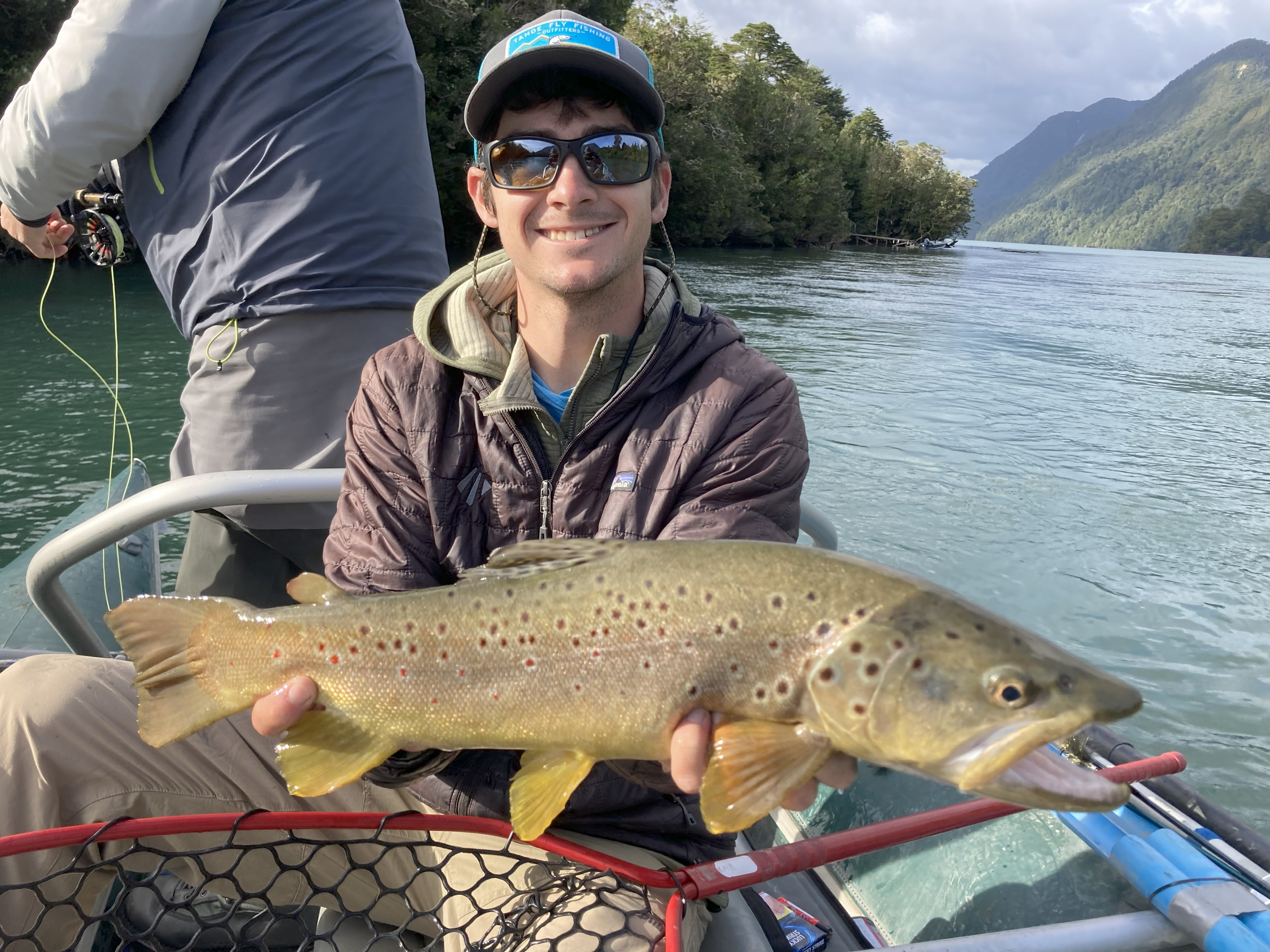 A boy smiling holding a fish on the river.