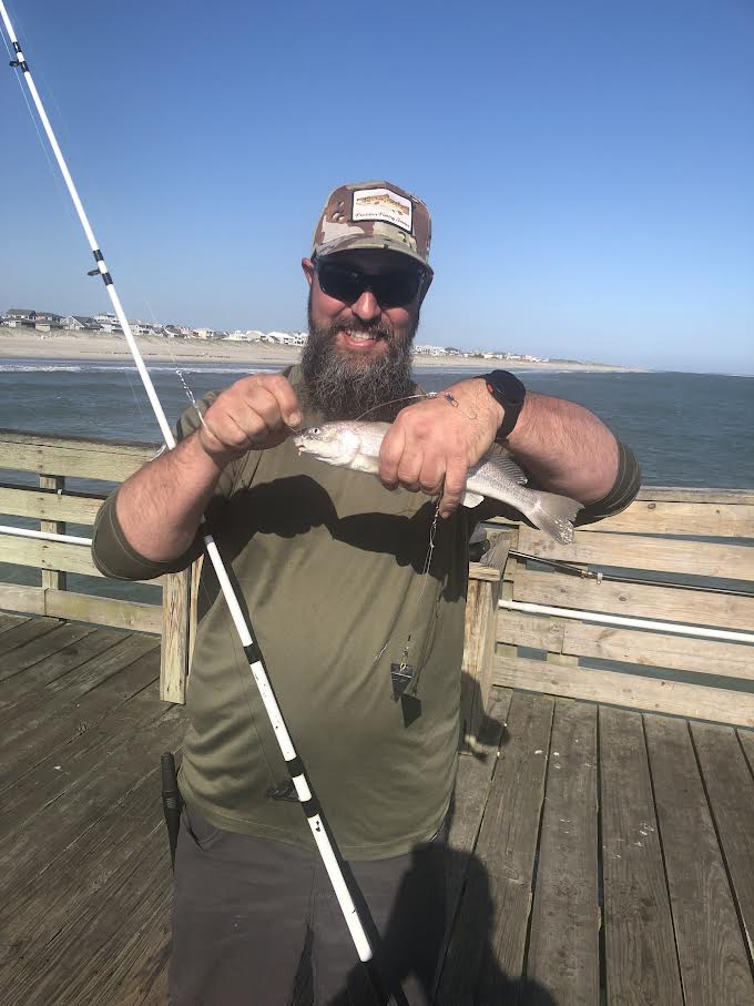 Man in camo hat with a fish on the pier.