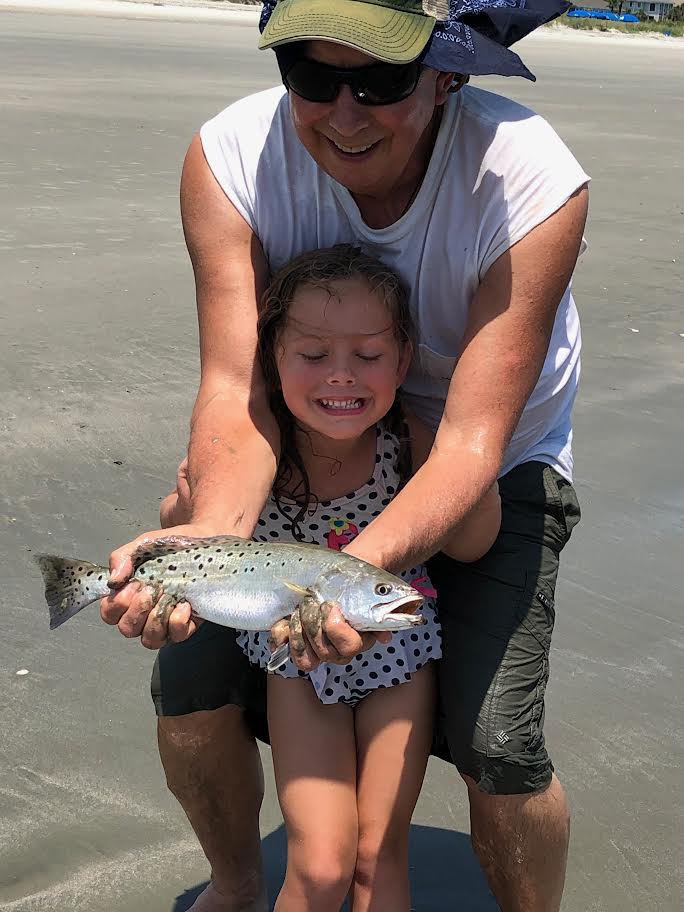 Man posing with girl on the beach with a fish.