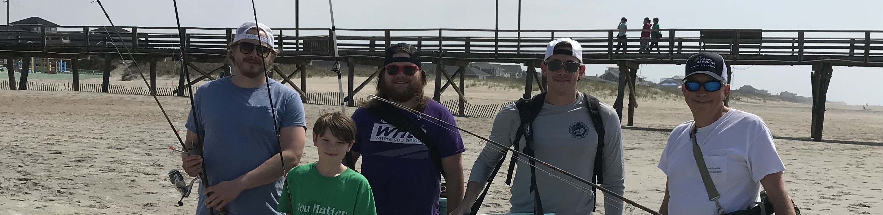 Man posing with fishing rods in front of scenic background.