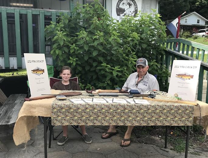 Man and grandson selling fishing books at a table.
